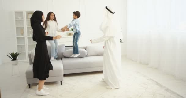 Joyeuse famille musulmane joyeuse dansant et s'amusant dans le salon à la maison pendant le confinement. Mère arabe et le père dansent avec petit fils et fille mignon. Petits enfants appréciant la musique avec des parents arabes — Video