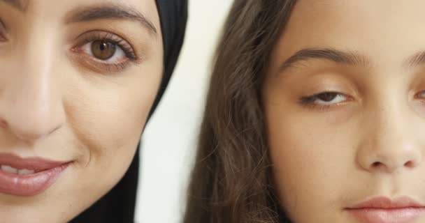 黒ヒジャーブの若い美しいアラブ人女性とかなり小さな女の子の半分の顔を閉じます。白地だ。肖像画。笑顔幸せなイスラム教徒の母親でheadcarfと魅力的な小さな娘. — ストック動画