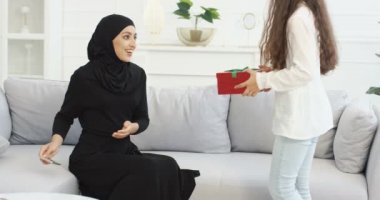 Küçük kızı tesettürlü Müslüman annesi ile arkası dönük geliyor. Abaya elbiseli Arap kadın kanepede oturuyor ve hediyesini kutuya koyuyor. Tatil, doğum günü ya da Anneler Günü hediyesi.