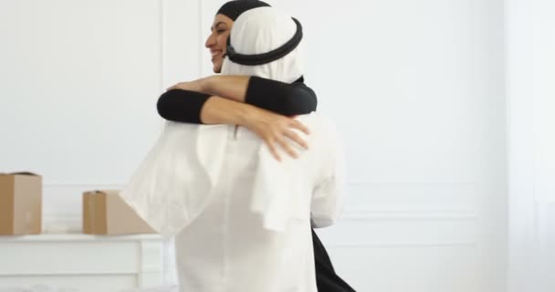 Happy just-married couple hugging and whirling in new house after moving in. Cheerful Arab husband in traditional kandura spinning wife in black hijab and embracing. Arabian man and woman Love concept — Stock Video