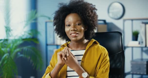 屋内作業場に座っている間に何かを説明する美しい若い女性労働者の肖像画。キャビネットで話しているかなり幸せなアフリカ系アメリカ人のオフィスの女の子の閉鎖。仕事のコンセプト — ストック動画