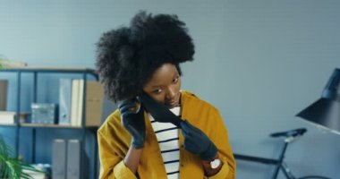 Ofiste koruyucu maske takan eldivenli güzel Afro-Amerikan kız portresi. Dolapta kameraya poz veren güzel bir bayan işçi. Karantinada çalış. Konsepti kapat