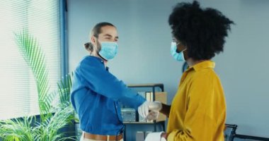 Tıbbi maskeli ve eldivenli kadın ve erkek melez işçilerin portresi ofiste dururken dirsekleriyle selam veriyor. Afrikalı Amerikalı güzel kız dolaptaki yakışıklı beyaz adamla konuşuyor.