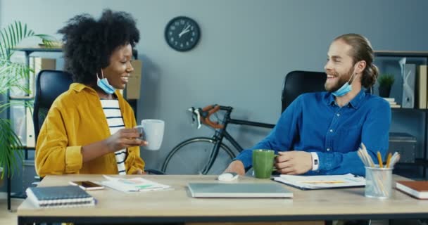 Weseli, wieloetniczni pracownicy mają przerwę na kawę siedząc w biurze. Ładna Afroamerykanka z filiżanką kawy rozmawiająca z mężczyzną. Przystojny biały mężczyzna sączy drinka i rozmawia z dziewczyną — Wideo stockowe