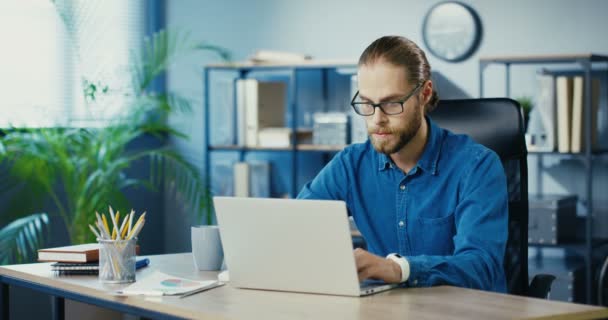 Blanc sérieux employé de bureau masculin tapant sur ordinateur portable tout en travaillant dans le cabinet. Bel homme occupé dans les lunettes de navigation sur l'ordinateur tout en étant assis à l'intérieur du lieu de travail. Concept d'entreprise — Video