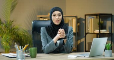 Başörtülü güzel Müslüman kadın ofisinde oturmuş kamerayla konuşuyor, öğretiyor ve anlatıyor. Kadın Arap iş blogcusu. Çevrimiçi webinar. İş kadını konuşuyor ve vlog kaydediyor