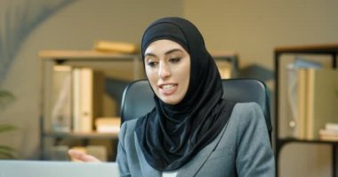 Geleneksel siyah tesettürlü neşeli müslüman kadın ofiste müşterisiyle bilgisayar başında web kamerasıyla konuşuyor. Arap bayan yönetici müşteriyle video kasette konuşuyor. Video sohbeti.