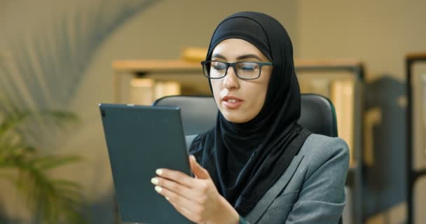 Arabische schöne Frau im schwarzen Hijab sitzt im Büro, tippt und scrollt auf dem Bildschirm des Tabletgeräts. Muslima gelangweilt Geschäftsfrau mit traditionellem Kopftuch surft auf Computer Araberin mit Brille — Stockvideo