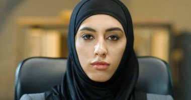 Kapalı mekanda siyah tesettürlü güzel müslüman kadının kadın yüzünü kapatın. Ofisteki kameraya gülümseyen siyah gözlü Arap çekici kadının portresi. Geleneksel türbanlı iş kadını.