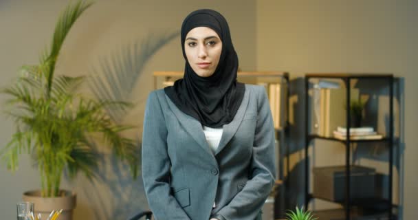 Portret foto van jonge mooie moslim vrouw in zwarte hijab staan in gezellig kantoor en glimlachend naar de camera. Mooie stijlvolle vrouwelijke manager werknemer in traditionele hoofddoek poseren. Arabische zakenvrouw. — Stockvideo