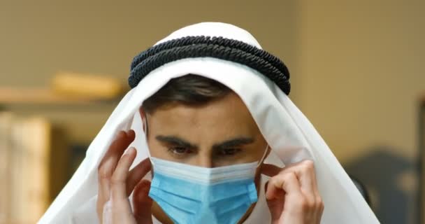 Zbliżenie młodego przystojnego muzułmanina w Kandurze zdejmującego maskę medyczną i uśmiechającego się w biurze. Arabski biznesmen w tradycyjnym stroju z uśmiechem. Portret mężczyzny w dishdashy. Koncepcja pandemii. — Wideo stockowe