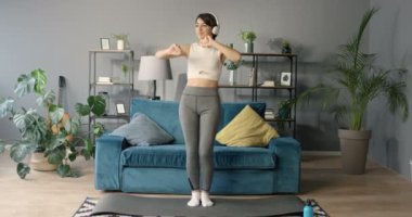 Kafkasyalı güzel bir kadın, kulaklıklı, spor yaparken müzik dinliyor ve rahat oturma odasında paspasın üzerinde dans ediyor. Evde en sevdiği şarkıyla sportif kadın ısınıyor..