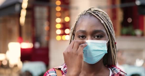非洲裔美籍年轻女子的画像，对着镜头笑，站在街上，摘下医疗面具。在室外与时尚漂亮的女性亲密接触。大流行性大肠癌概念. — 图库视频影像