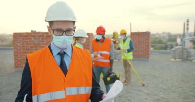 Kafkasyalı genç yatırımcı Hemet ve tıbbi maskenin portresi. İnşaat planı ellerindeydi. Erkek mühendis ya da mimar salgında yapı kenarı oluşturmada.