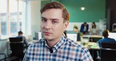 Sarışın ve mavi gözlü genç adamın yakın portresi kameraya bakıp gülümsüyor. Ofis arka planda.