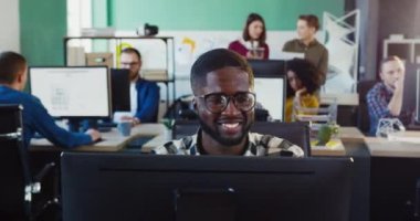 Bilgisayarda çalışan gözlüklü genç Afrikalı Amerikalı adamın portresi. Ofiste online danışman, programcı, tasarımcı veya geliştirici olarak çalış.