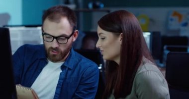 İki genç işçi ofiste otururken proje üzerinde birlikte çalışıyorlar. Yakışıklı adam ve kadın notları kontrol ediyor ve bilgisayar ekranına bakıyor..