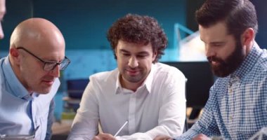 Yuvarlak masa başında oturan bir grup yetişkin erkek profesyonel kağıt belgeler kullanarak yeni proje üzerinde kafa patlatıyorlar..