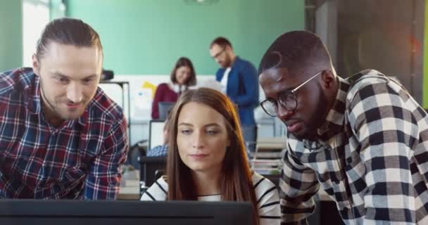 Tres jóvenes: dos hombres y una mujer, trabajando en el ordenador en coworking. Equipo multinacional discute proyecto en oficina. — Vídeos de Stock