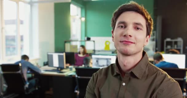 Primer plano retrato de joven trabajador de oficina guapo en camisa marrón. Elegante hombre sonriendo a la cámara mientras está de pie en la oficina. — Vídeos de Stock