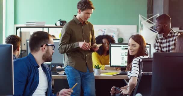 Jovens profissionais da equipe discutindo tarefas uns com os outros enquanto estão sentados no escritório. Os colegas comunicam-se durante o intervalo. Trabalho em equipa no co-trabalho. — Vídeo de Stock