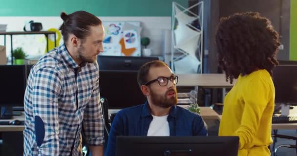 Két fehér férfi és egy afro-amerikai nő sárga pulóverben megbeszélik az irodában álló projekttel kapcsolatos munkát.. — Stock videók