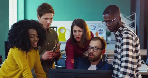 Young multinational team of specialists gathered in office near computer for brainstorming session. Team work. Take notes. Discuss workflows. — Stock Video