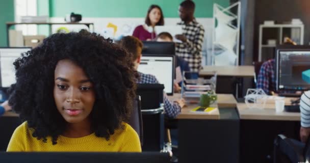 Porträt einer jungen afrikanisch-amerikanischen Frau mit lockigem Haar, die im Büro sitzt und am Computer arbeitet. Konzept der Bürokauffrau. — Stockvideo