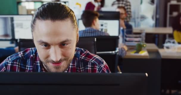 Közeli kép fiatal fehér férfi kockás ing dolgozik a számítógép, és megoldja a munka problémák, miközben ül az irodában. — Stock videók