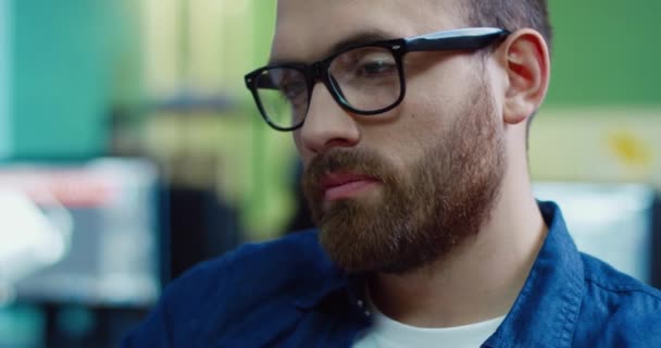 काम करते समय मॉनिटर स्क्रीन को देखते हुए चश्मे में दाढ़ी वाले युवा सुंदर काकेशियन आदमी को बंद करें . — स्टॉक वीडियो