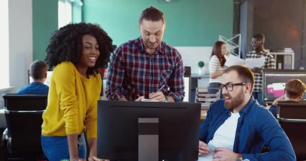 Três trabalhadores de escritório: uma menina e dois homens, rindo olhando para a tela do computador. Jovem equipe brainstorming sobre projeto de design. — Vídeo de Stock