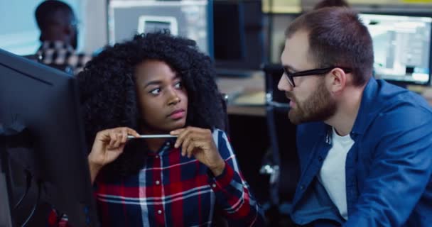 Two employees: Caucasian man and African-American woman sitting in office working on joint task. Professional explains details of project to newcomer. — Stock Video