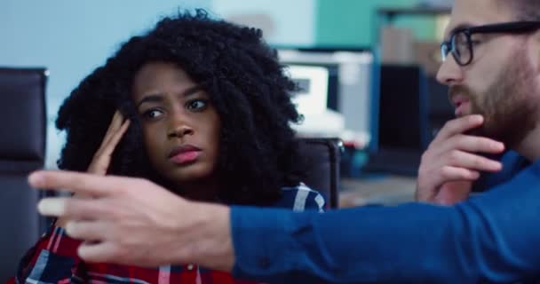 Close up of two workers: caucasian man and african american woman with curly hair sitting in office working on joint task. Brainstorming together. — Stock Video