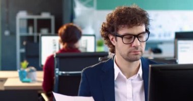 Takım elbiseli ve gözlüklü bir ofis çalışanının portresi masada oturuyor ve kağıt belgeler okuyor. Eş zamanlı çalışma.