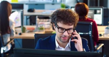 Ofis çalışanının gözlüklü ve takım elbiseli portresi masada oturuyor ve cep telefonuyla müşteriyle kibarca konuşuyor..