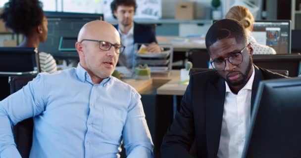 Stilig ung afrikansk amerikansk man i kostym och glasögon och senior affärskonsult arbetar med uppgiften kontrollera varandra arbete. — Stockvideo