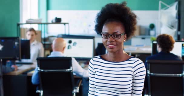 Potret wanita Afrika-Amerika muda dengan rambut keriting. Gadis cantik berdiri di kantor dengan tangan disilangkan di dadanya dan tersenyum. — Stok Video