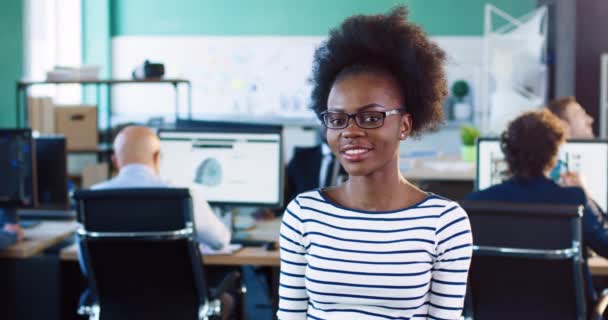 Tutup potret muda african american wanita dalam gelas dengan rambut keriting. Gadis cantik berdiri di kantor tersenyum melihat kamera. — Stok Video