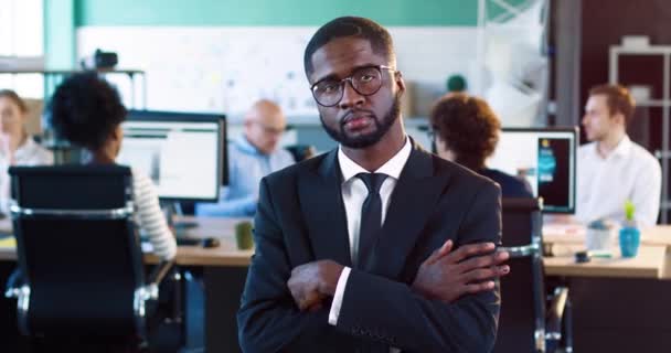 Porträt eines gutaussehenden afroamerikanischen Mannes in schwarzem Anzug und Brille. Junger Mann verschränkt die Arme über der Brust und lächelt in die Kamera. — Stockvideo