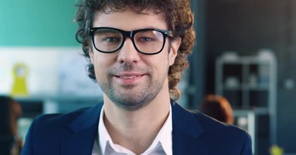 Close up portret młodego, białego biznesmena w garniturze z okularami uśmiechniętymi do kamery stojącej w biurze. — Wideo stockowe