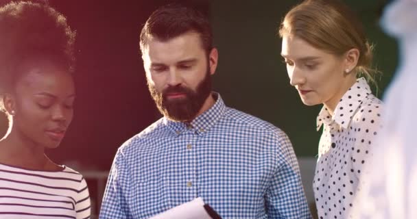 Un homme barbu caucasien et deux jeunes femmes regardent dossier avec dossier. Un groupe multinational travaille ensemble sur un projet commun. — Video