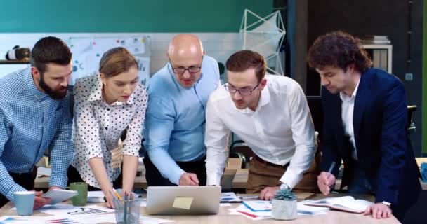 眼鏡をかけたシニア・ビジネス・ワーカーが事務所で業務プロセスを管理する。テーブルの周りに立っている問題を議論し、文書を頑丈な専門家の若いチーム. — ストック動画
