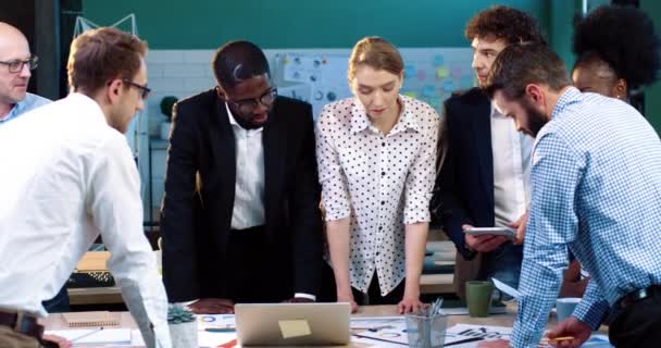 Multinationaal team: vijf mannen en twee vrouwen, brainstormend op kantoor en samen documenten studerend aan één grote tafel. Teamwork. — Stockvideo