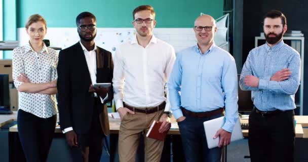 Porträtt av framgångsrika multinationella team av yrkesverksamma: fyra män och en kvinna som står på kontoret poserar för kameran leende. — Stockvideo