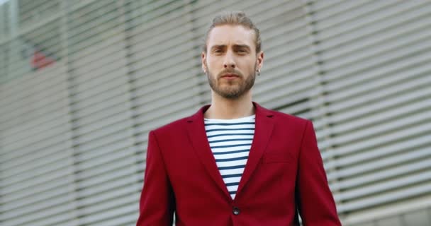 Retrato de hombre guapo joven caucásico en chaqueta roja mirando a la cámara y sonriendo alegremente al aire libre. Elegante chico alegre y guapo en el edificio exterior. — Vídeos de Stock