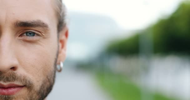 Primer plano de media cara de joven caucásico alegre guapo hombre con oído en la oreja sonriendo a la cámara y mirando directamente al aire libre. Retrato de hombre guapo con estilo feliz. — Vídeos de Stock