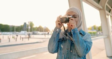 Geleneksel türbanlı, genç, güzel, Müslüman bir kadın sokaktaki klasik fotoğraf makinesinde fotoğraf çekiyor. Şehirde dikilirken fotoğraf çeken Arap tesettürlü bir kadın.