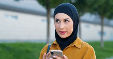 Siyah başörtüsü takmış Arap genç ve güzel bir kadın sokakta dikiliyor ve akıllı telefondan mesaj yolluyor. Sivri dilli, tesettürlü ve cep telefonuyla kayan bir müslüman kadın. Sohbet. Açık hava..