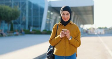 Siyah tesettürlü Müslüman güzel bir kadın sokakta yürüyor ve cep telefonunu dinliyor ya da kaydırıyor. Arabistan 'ın güzel kadını şehirde geziniyor ve dışarıda cep telefonundan mesaj atarken sohbet ediyor.