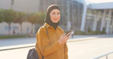 Sokakta kameraya gülümseyen siyah tesettürlü müslüman genç bir kadının portresi. Arabistan 'ın güzel bayanları dışarıda cep telefonuyla mesajlaşıp sohbet ediyorlar..